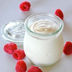 a glass jar filled with yogurt and raspberries next to another jar