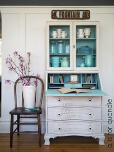 an old china cabinet is painted white and has pink flowers in the vase next to it