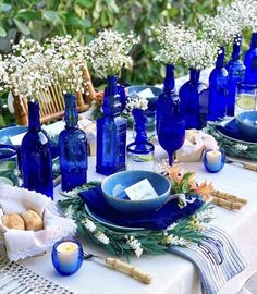 a table set with blue glass bottles and flowers on top of it, along with other items