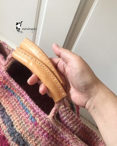 a hand holding a piece of leather in front of a white door with a pink and blue striped blanket