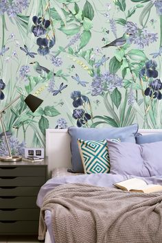 a bed sitting under a green wallpaper covered in blue and purple flowers next to a night stand