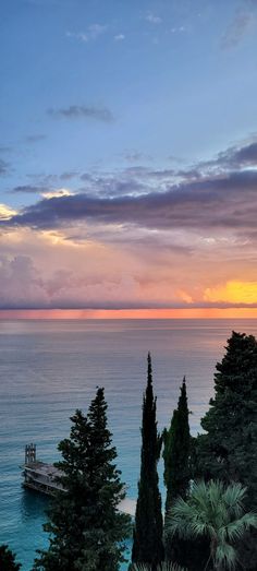 the sun is setting over the ocean with trees and a dock in the foreground