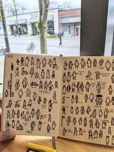 an open book with people drawn on it sitting on a table next to a window