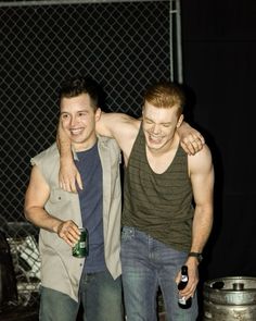 two young men standing next to each other holding beer bottles and smiling at the camera