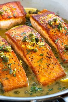 four salmon fillets in a pan with lemons and capers