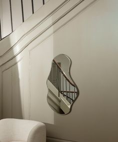 a white chair sitting under a mirror next to a stair case