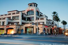 an intersection with traffic lights, palm trees and a building in the background at dusk