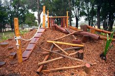 an outdoor play area made out of wood logs and sticks with ropes on top, surrounded by trees