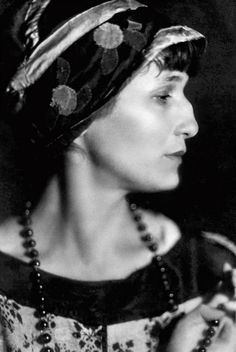 an old photo of a woman wearing a hat and beaded necklaces, with her eyes closed