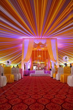 the interior of a wedding venue decorated in orange, yellow and white draping