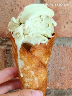 a hand holding an ice cream cone in front of a brick wall