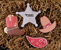 three decorated cookies with cowboy hats and boots on top of some wood shavings