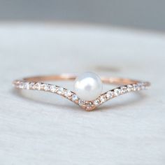 a white pearl and diamond ring sitting on top of a table