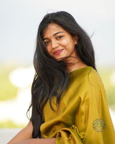 a woman with long black hair wearing a yellow sari and smiling at the camera