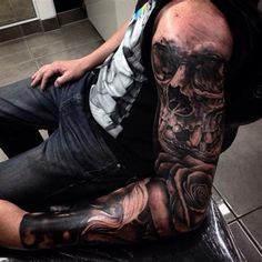 a man sitting on top of a chair covered in black and grey ink with a skull tattooed on his arm