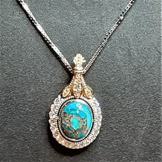 "An oval blue turquoise cabochon veined with copper is set in a bezel surrounded by a diamond halo in 14k white gold. The pendant bail is a diamond-studded yellow gold fleur-de-lis shape. The pendant measures about 28mm (or a little over 1\") long including the bail by 16mm (about 5/8\") wide. This pendant comes with a white gold box chain with a lobster clasp in your choice of 16\", 18\", or 20\" length Turquoise Dimensions11x9mm EnhancementNatural ColorMedium to light blue; copper matrix Cut G Turquoise Cabochon Necklace For Formal Occasions, Elegant Round Turquoise Cabochon Necklace, Formal Turquoise Cabochon Necklace, Luxury Turquoise Cabochon Necklace, Bezel Set Cabochon, Pendant Bail, Clover Ring, White Sapphire Engagement Ring, Pendant Bails