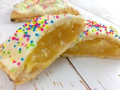 two pastries with white frosting and colorful sprinkles on them sitting on a wooden surface