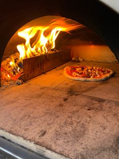 two pizzas cooking in an outdoor oven with flames coming from the top and bottom