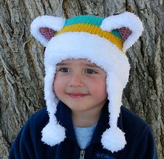 a young boy wearing a knitted hat with ears on top of his head, standing in front of a tree