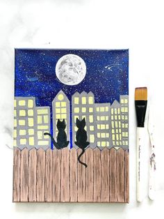 two black cats sitting on top of a wooden fence under a full moon with city lights in the background