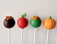 four cake pops with different colored frosting and decorations on them are lined up against a white wall