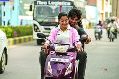 a man and woman riding on the back of a red scooter down a street