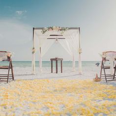 an outdoor wedding setup on the beach with yellow flowers and white draping over it