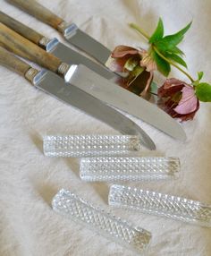 three knives and some flowers on a white table cloth next to it's contents