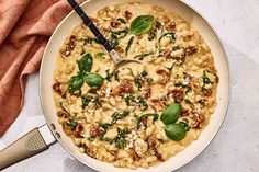 a pan filled with pasta and spinach on top of a white table cloth next to a spatula