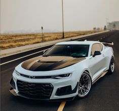 a white chevrolet camaro is parked on the side of the road in front of an empty highway