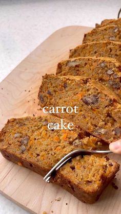 someone is cutting up some carrot cake on a wooden board with a knife and fork