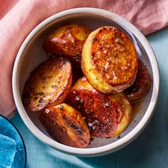 a white bowl filled with cooked potatoes on top of a blue cloth next to a fork