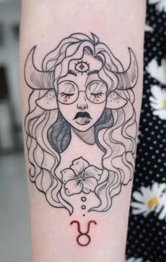 a woman's face with horns and flowers on her arm is depicted in this tattoo design