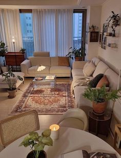 a living room filled with furniture next to a tall window covered in curtains and plants