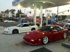 three cars are parked at a gas station, one is red and the other is white