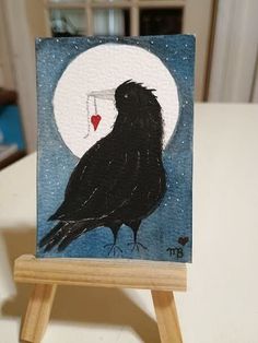 a small easel with a painting of a black bird sitting on top of it