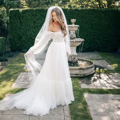 a woman in a white wedding dress standing next to a fountain and wearing a veil