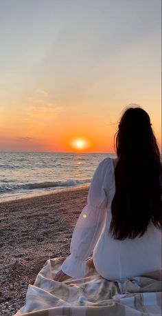 a woman sitting on the beach watching the sunset