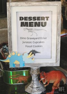 there is a sign that says dessert menu next to two dinosaur cupcakes and a cookie tin