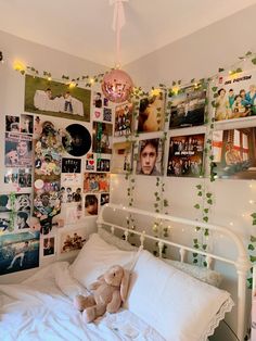 a white bed topped with lots of pictures and lights next to a wall covered in photos