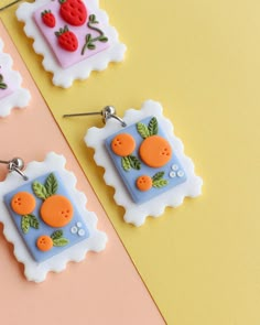 three square shaped earrings with buttons and leaves on them sitting on a yellow and pink background