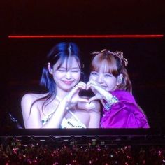 two young women standing next to each other in front of a large screen at a concert