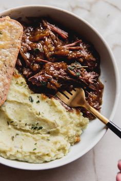 a white bowl filled with mashed potatoes and meat next to a piece of bread