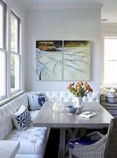 a white couch sitting next to a table in a living room under two large windows