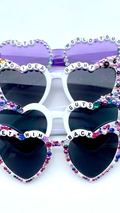 two heart shaped sunglasses with words written on the front and sides, both decorated with crystals