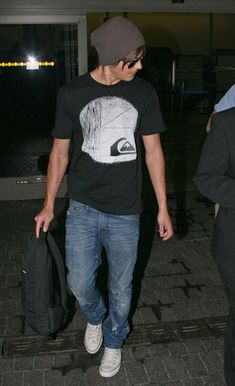 a young man carrying a black bag while walking through an airport terminal with another person in the background