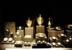 there are many silver items on display in the dark room, including cups and saucers