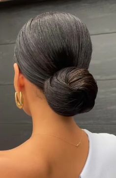 a woman with her hair in a low bun wearing gold hoop earrings and a white shirt