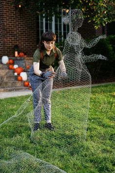 a woman standing next to a wire sculpture on top of a green grass covered field