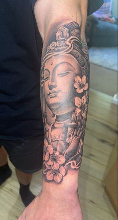 a person's arm with a buddha tattoo on it and flowers in the background